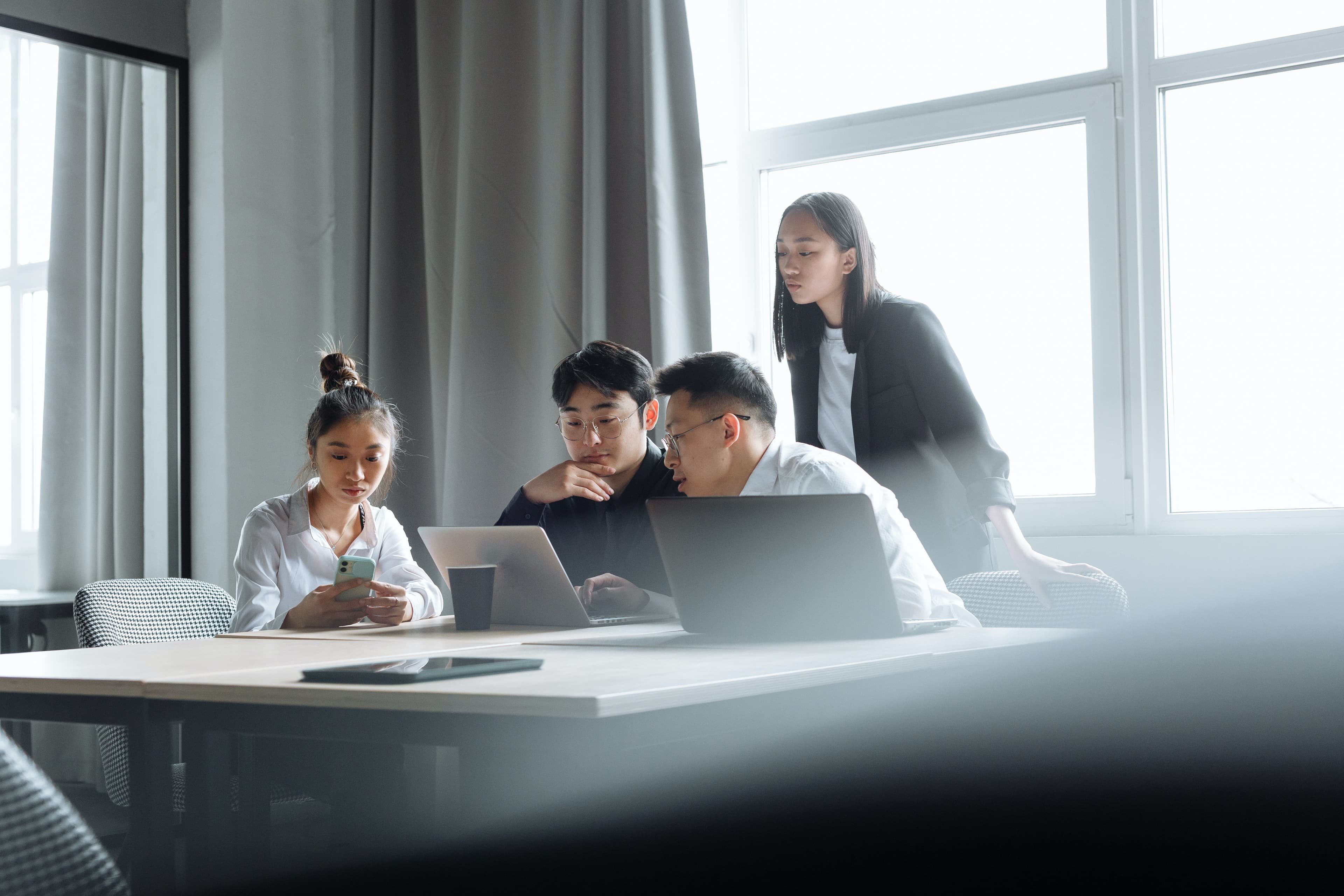 A group of professionals collaborates in a modern office space, reviewing documents on laptops and discussing project plans, representing innovation and teamwork in the construction industry.